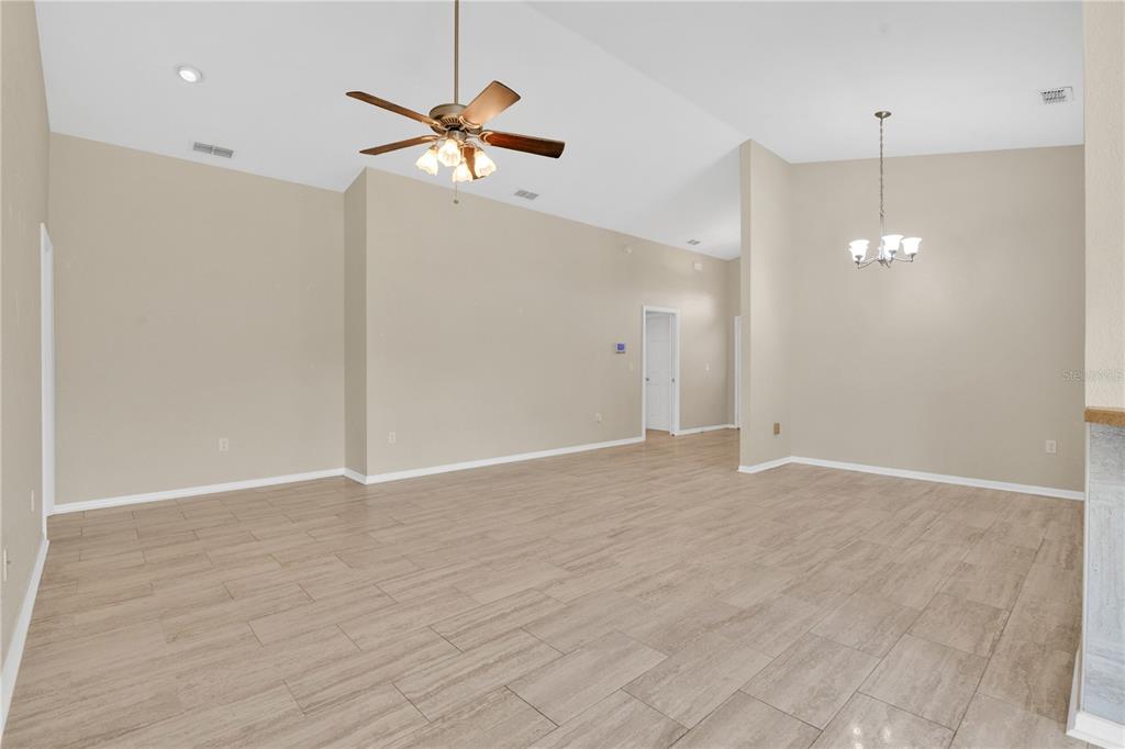 An empty living and dining area features vaulted ceilings, light-colored walls, and wood-look tile flooring — 4919 ST JAMES DRIVE, WINTER HAVEN, FL