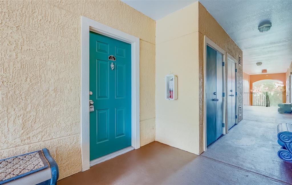 A teal front door with number 136 sits next to a fire extinguisher and utility closet — 2705 VIA MURANO UNIT 136, CLEARWATER, FL