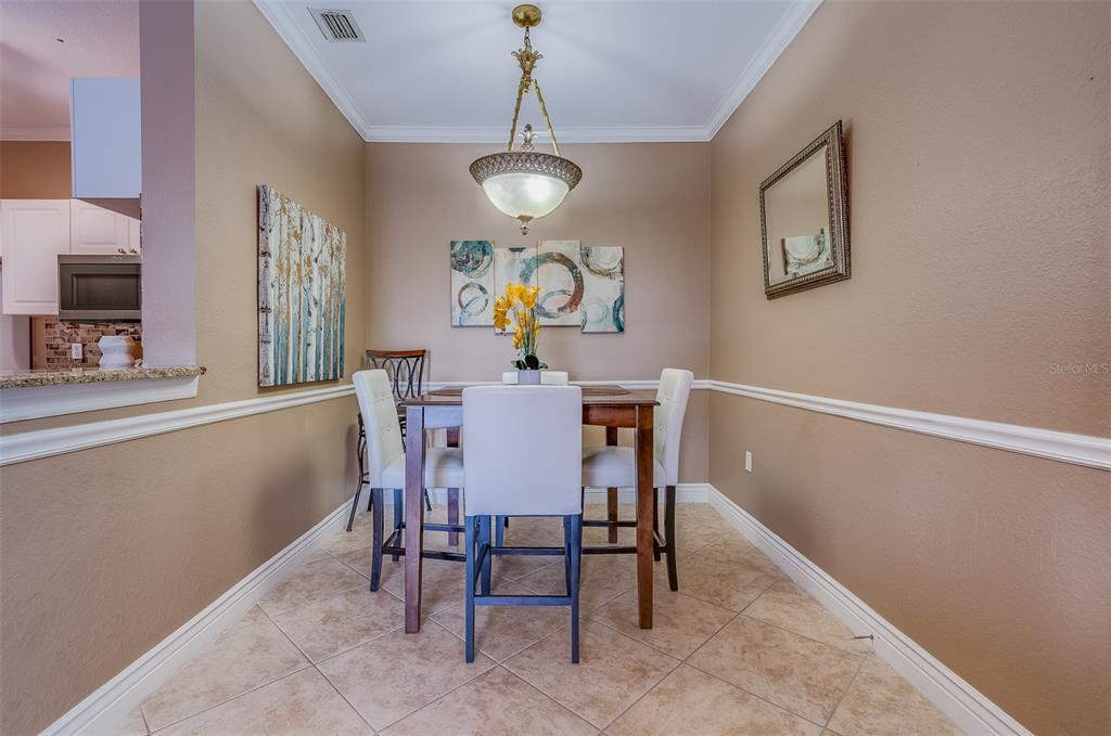 A dining area features a wooden table with four white chairs and a pendant light — 2705 VIA MURANO UNIT 136, CLEARWATER, FL