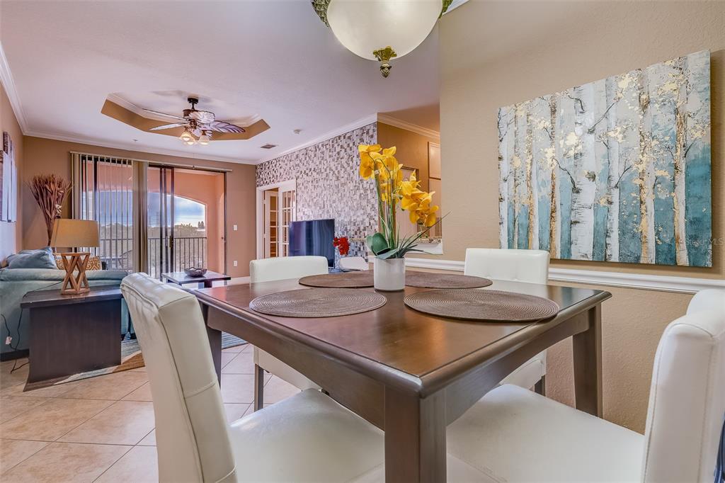 A dining area with a wooden table and white chairs sits before a living room — 2705 VIA MURANO UNIT 136, CLEARWATER, FL