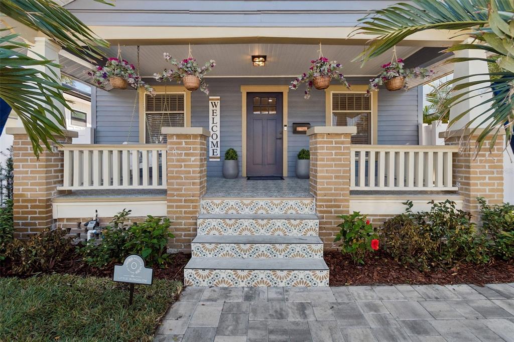 A front porch with patterned tile stairs, brick columns, hanging flower baskets, and a blue door — 322 11TH AVENUE N, ST PETERSBURG, FL