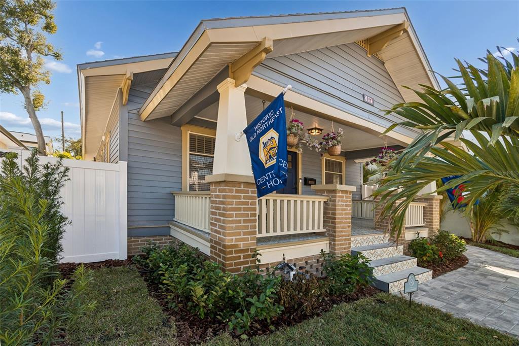 A blue bungalow features a covered front porch with brick columns and a decorative flag — 322 11TH AVENUE N, ST PETERSBURG, FL