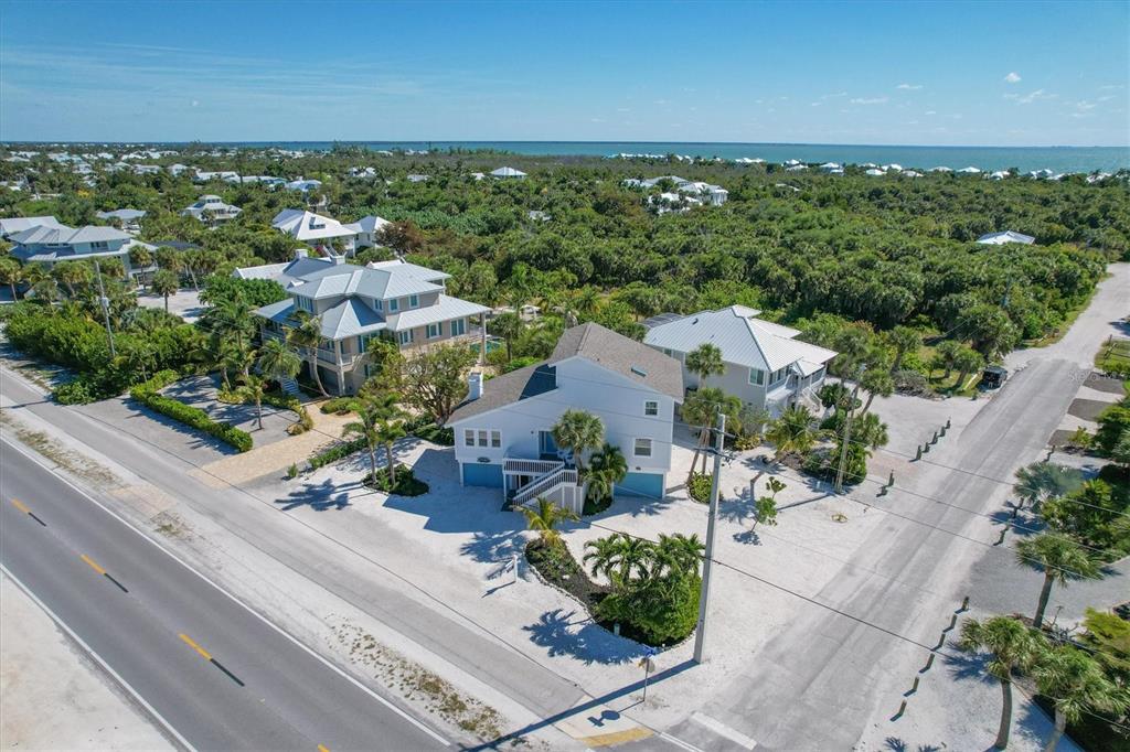 An aerial view shows three multi-story coastal houses surrounded by lush vegetation near the ocean — 401 LAFITTE STREET, BOCA GRANDE, FL