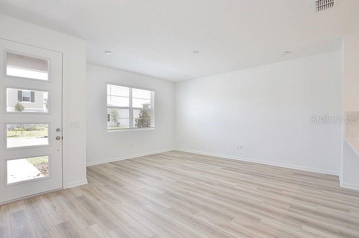 An empty room features light wood-look flooring, white walls, and a modern front door — 11420 SUNSAIL AVENUE, ORLANDO, FL