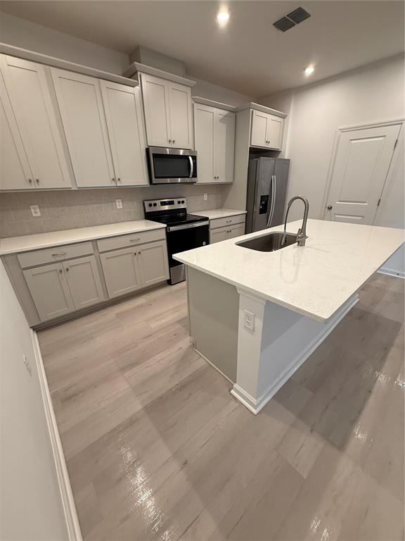 A modern kitchen features light gray cabinets, white countertops, stainless steel appliances, and wood-look flooring — 11420 SUNSAIL AVENUE, ORLANDO, FL