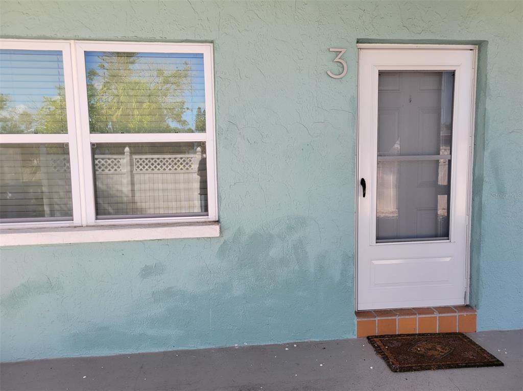 The exterior of a light blue building features a white door labeled with number three — 7650 COQUINA WAY UNIT 3, ST PETE BEACH, FL