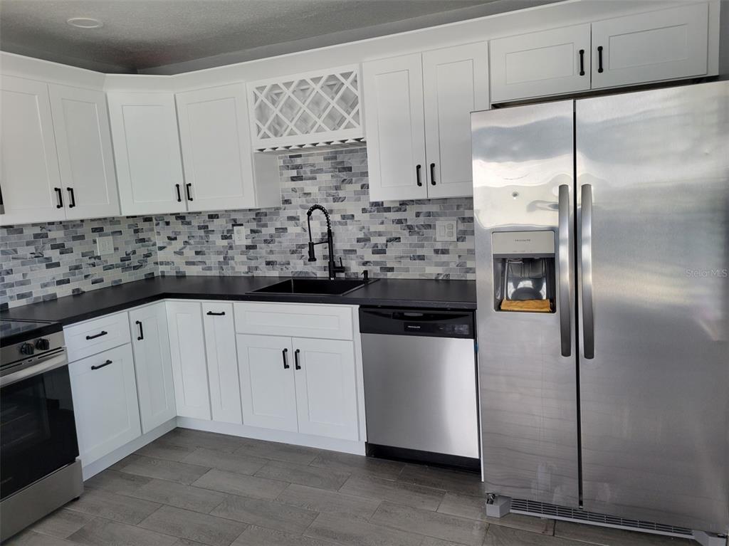 A kitchen with white cabinets, black countertops, stainless steel appliances, and a gray tiled backsplash — 7650 COQUINA WAY UNIT 3, ST PETE BEACH, FL