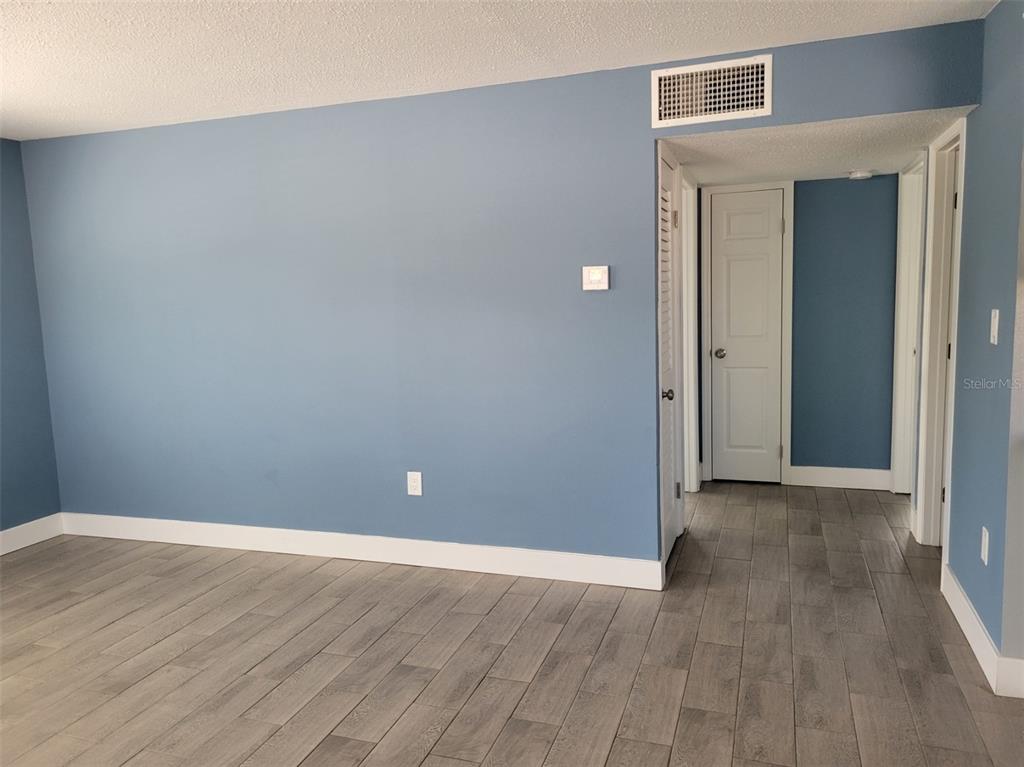 A room with blue walls, gray wood-look flooring, and a doorway leading to a hallway — 7650 COQUINA WAY UNIT 3, ST PETE BEACH, FL