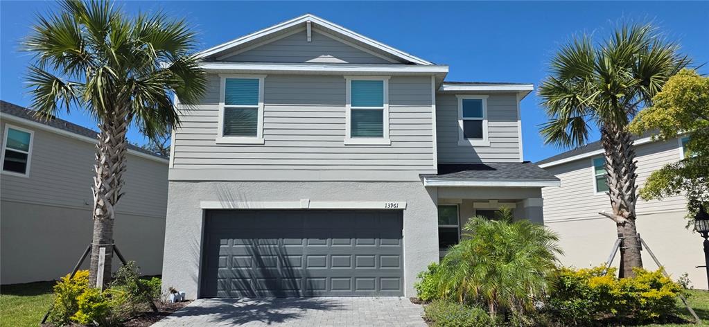 A two-story house with a gray garage door, light siding, and a paved driveway — 13961 LILAC SKY TERRACE, BRADENTON, FL