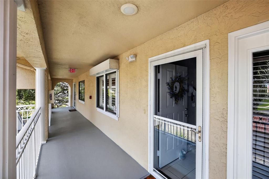 An outdoor covered walkway features a white railing, beige stucco walls, and a screen door — 443 BOUCHELLE DRIVE UNIT 302, NEW SMYRNA BEACH, FL