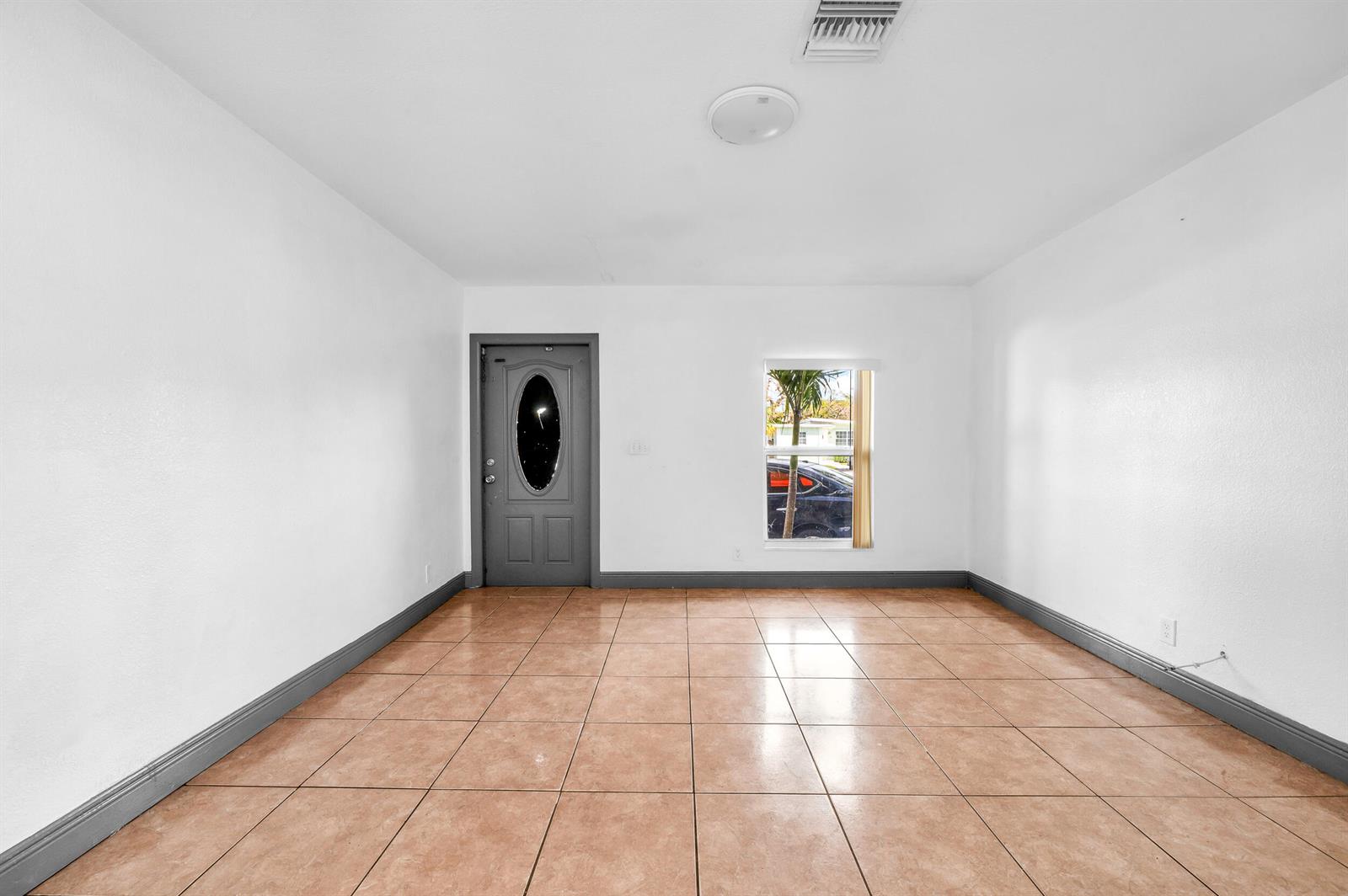 An empty room with white walls, tan tile flooring, a gray door, and one window — 124 SW 10th Avenue, Boynton Beach FL 33435, BOYNTON BEACH, FL