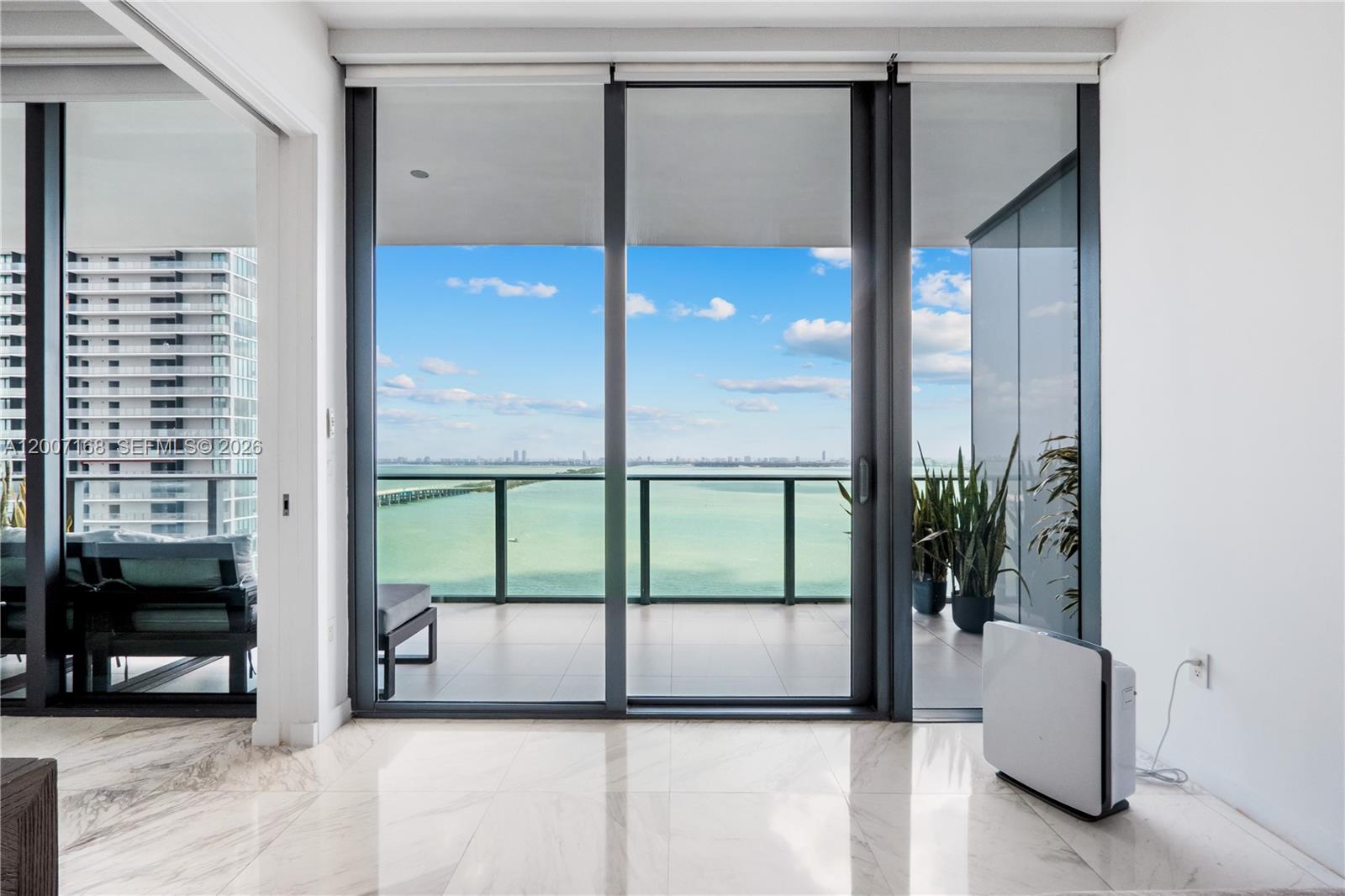 A room with marble floors features floor-to-ceiling glass doors opening to a balcony overlooking water — 480 NE 31st St # 2405, Miami FL 33137, MIAMI, FL