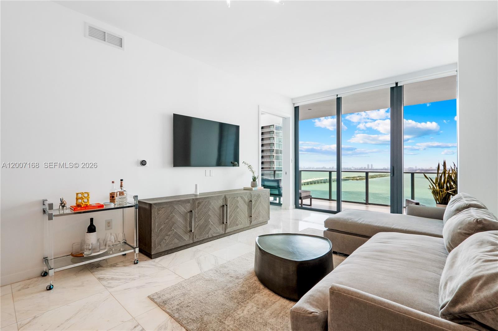 A modern living room features a grey media console, a sectional sofa, and floor-to-ceiling windows — 480 NE 31st St # 2405, Miami FL 33137, MIAMI, FL
