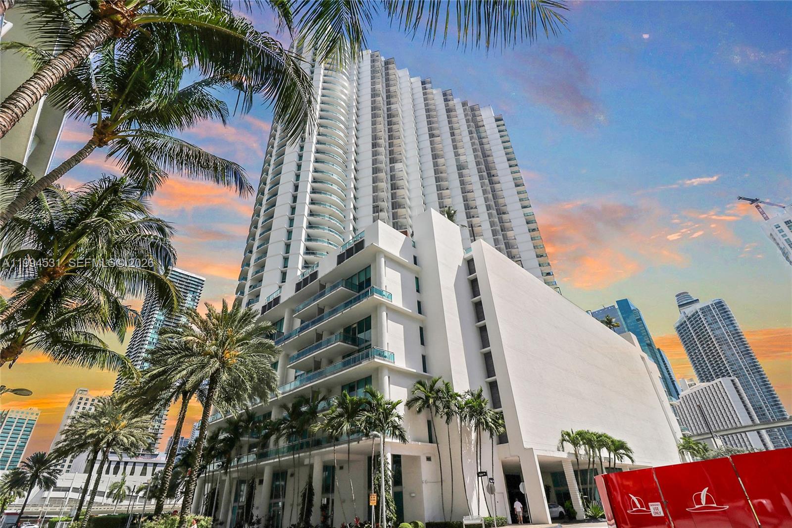A low-angle view of a tall white modern residential skyscraper surrounded by palm trees — 350 S Miami Ave # 4110, Miami FL 33130, MIAMI, FL