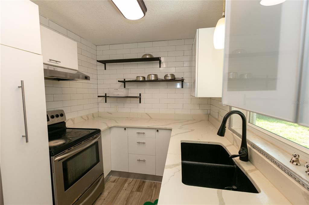A modern kitchen features white cabinets, open shelving, a black sink, and marble-patterned countertops — 3562 BOUGAINVILLEA DRIVE, WINTER PARK, FL