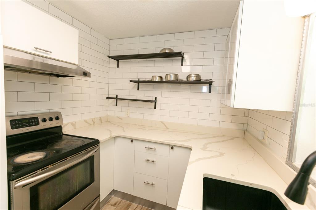 A kitchen features white cabinets, subway tile backsplash, open shelving, and light-colored stone countertops — 3562 BOUGAINVILLEA DRIVE, WINTER PARK, FL