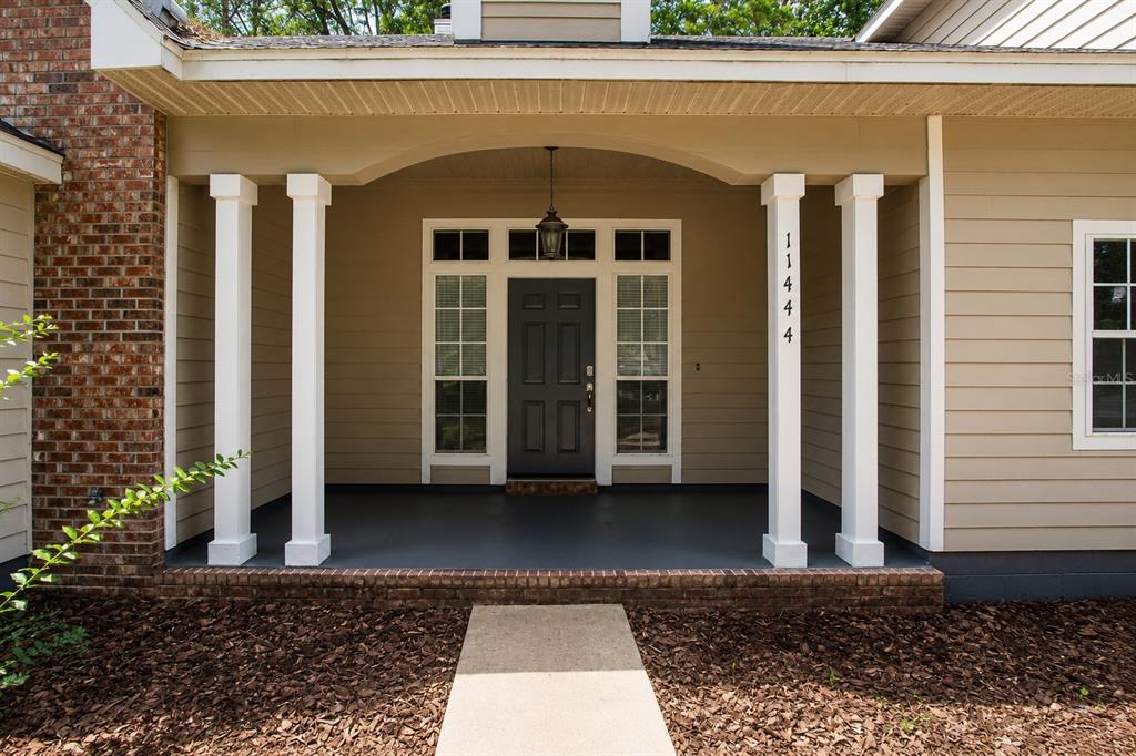 A covered front porch features white columns, a dark door, and brick accents — 11444 NW 18TH LANE, GAINESVILLE, FL