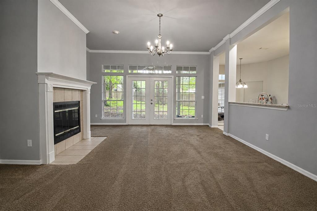 A living room features a fireplace, carpeted flooring, a chandelier, and a view of the backyard — 11444 NW 18TH LANE, GAINESVILLE, FL