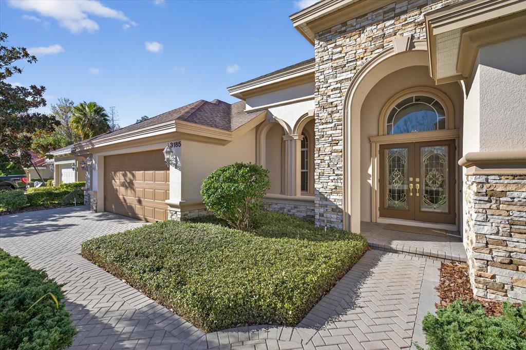 A front view of a house with a stone facade, arched entryway, and paved driveway — 3185 BURBERRY STREET, TARPON SPRINGS, FL