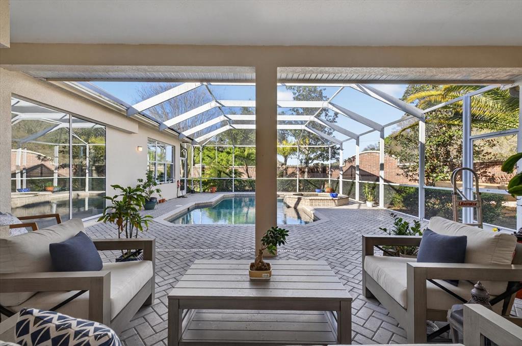 A covered patio overlooks a screened-in swimming pool and hot tub with brick pavers — 3185 BURBERRY STREET, TARPON SPRINGS, FL