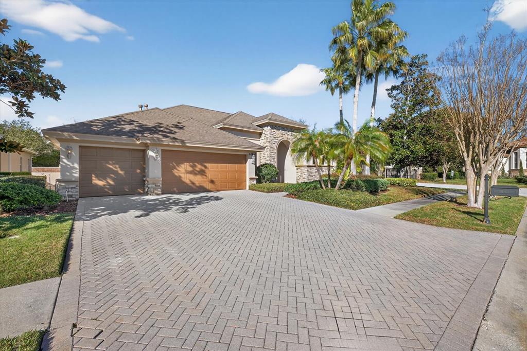 A single-story house with a stone facade, a three-car garage, and a herringbone-patterned paver driveway — 3185 BURBERRY STREET, TARPON SPRINGS, FL