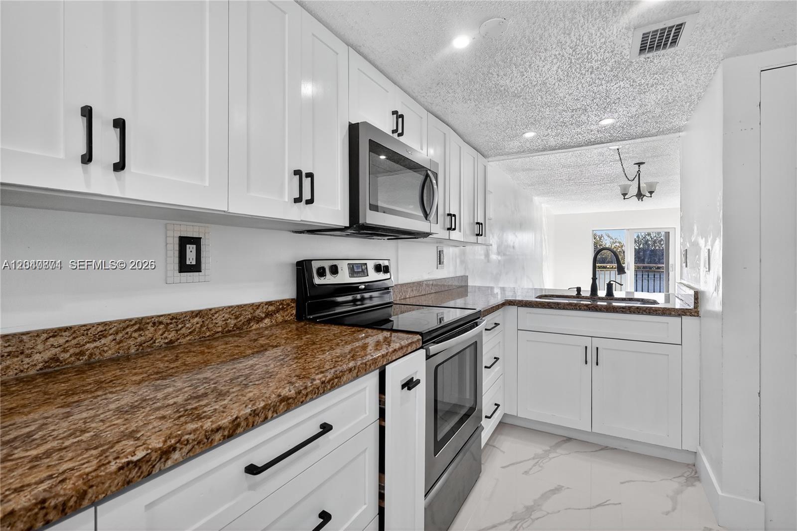 A kitchen features white cabinets, granite countertops, stainless steel appliances, and white marble-look flooring — HIALEAH GARDENS, FL