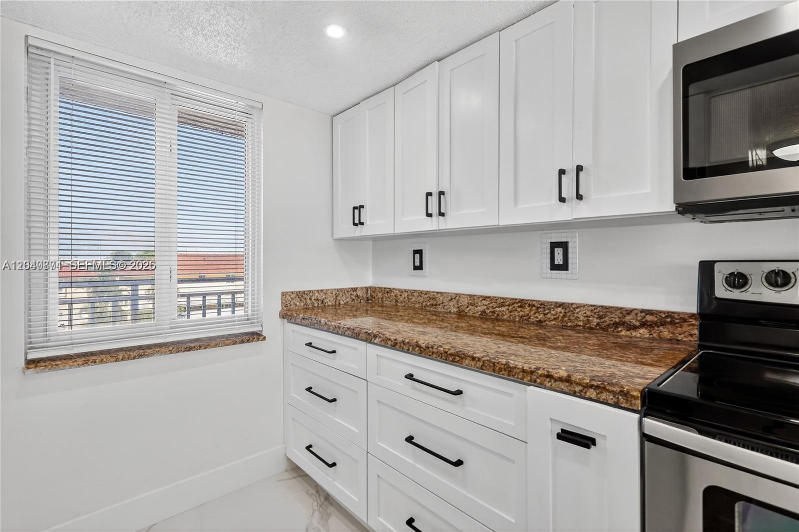 A kitchen features white cabinets, granite countertops, stainless steel appliances, and a window with blinds — HIALEAH GARDENS, FL