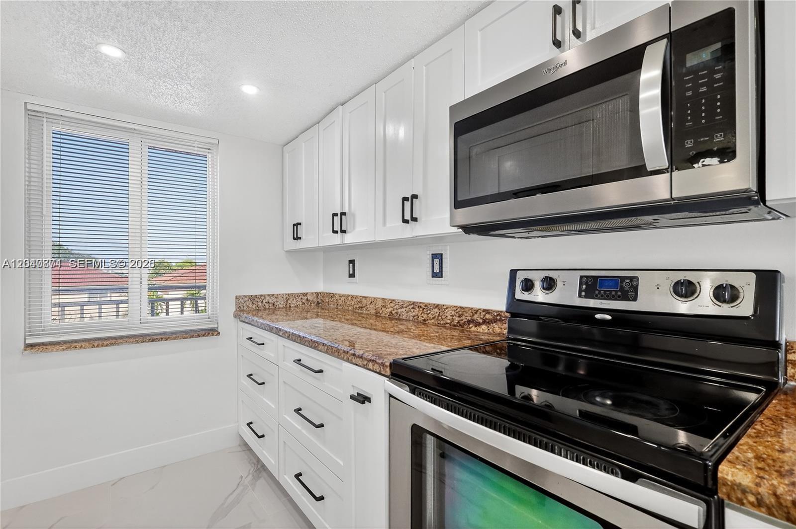 A kitchen features white cabinets, granite countertops, stainless steel appliances, and a window with blinds — HIALEAH GARDENS, FL