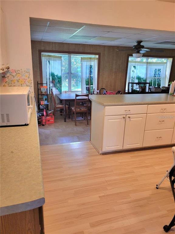 A kitchen with light wood-look flooring and white cabinets overlooks a dining area with wood-paneled walls — 5400 SAN JUAN BOULEVARD, ORLANDO, FL