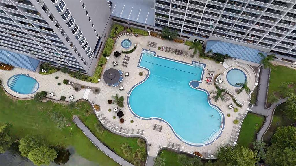 An aerial view shows a large swimming pool, two hot tubs, and surrounding apartment buildings — 13415 BLUE HERON BEACH DRIVE UNIT 407, ORLANDO, FL