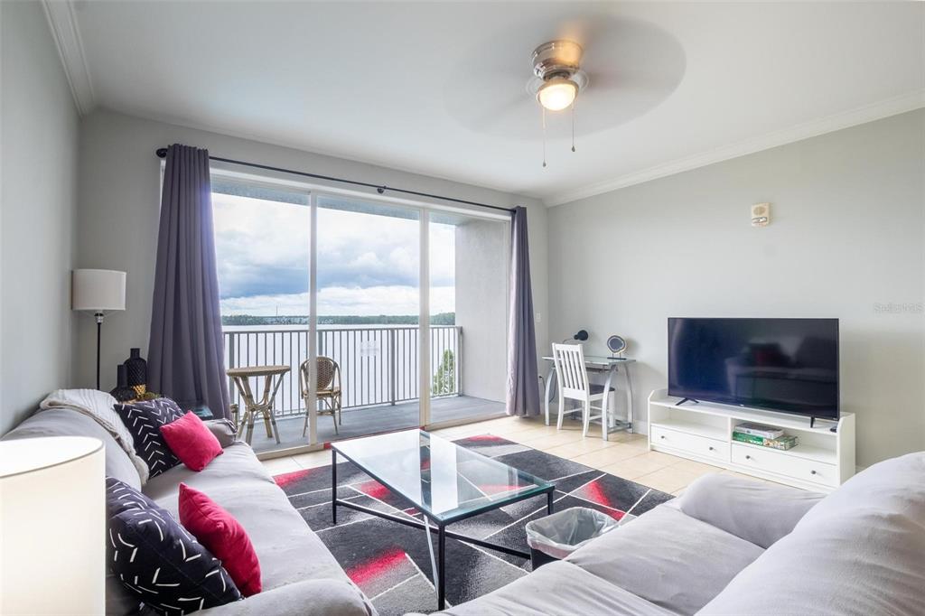 A living room features a glass coffee table, a television, and a balcony overlooking water — 13415 BLUE HERON BEACH DRIVE UNIT 407, ORLANDO, FL