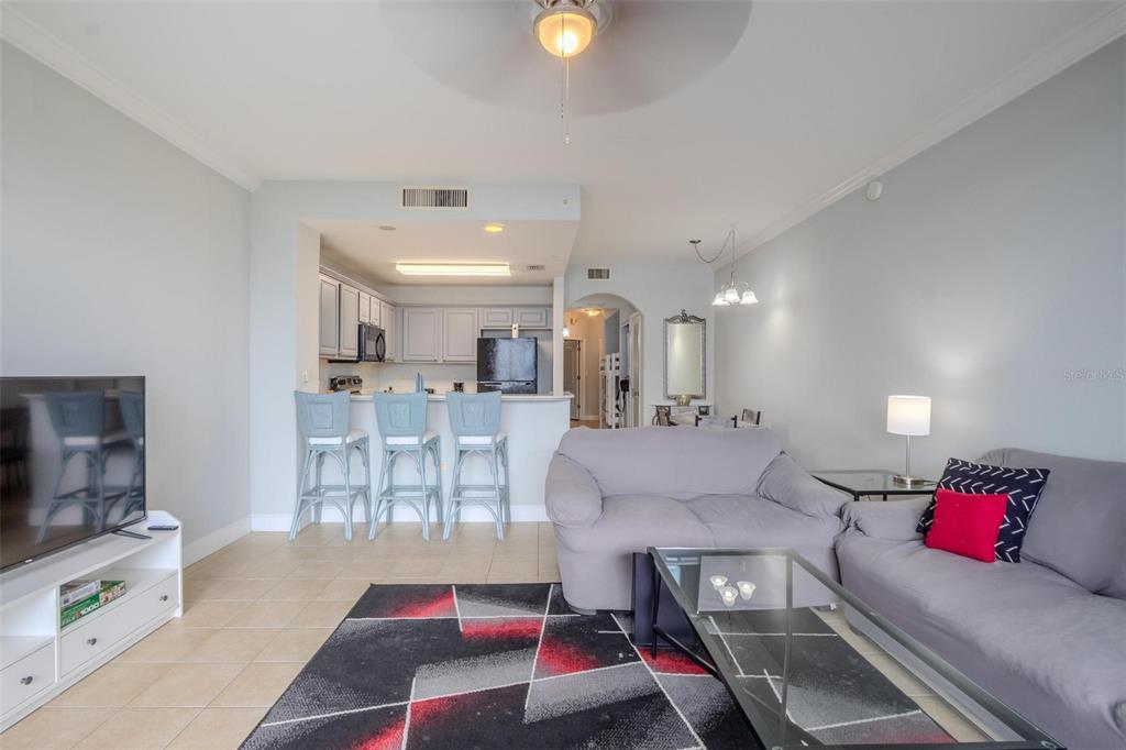 A living room with a kitchen island, bar stools, and a patterned area rug — 13415 BLUE HERON BEACH DRIVE UNIT 407, ORLANDO, FL