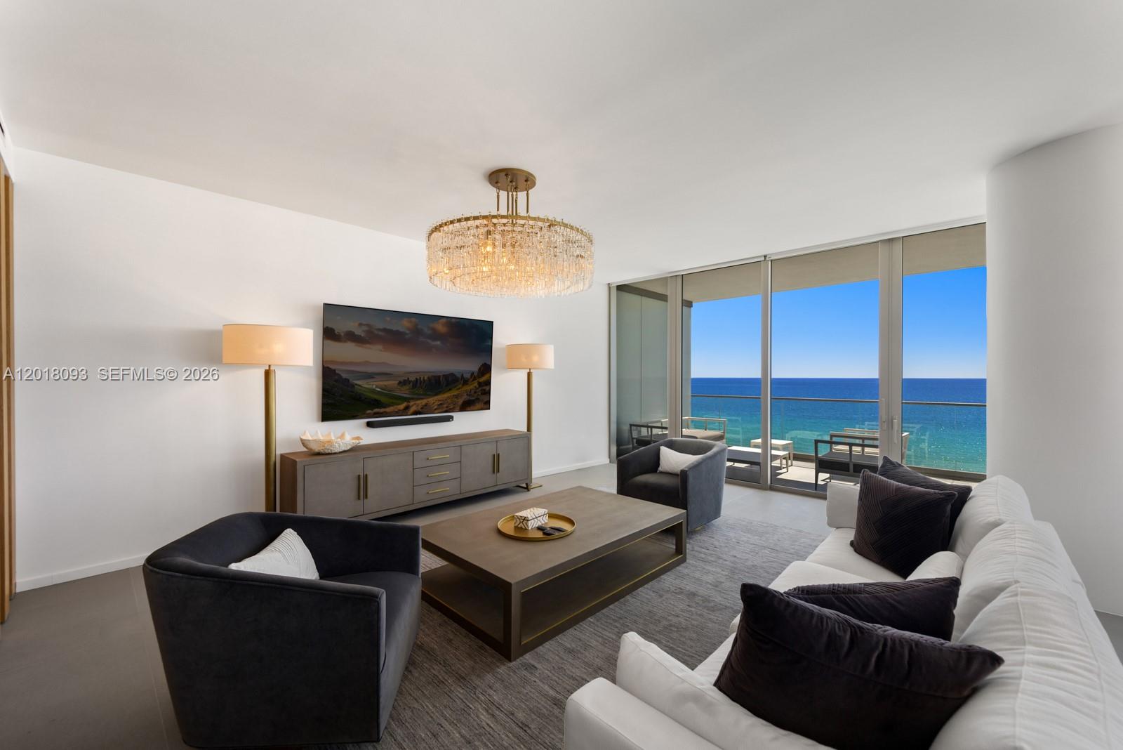 A living room features a crystal chandelier, a television, and a balcony overlooking the ocean — 2000 S Ocean Dr # 7B, Hallandale Beach FL 33009, HALLANDALE BEACH, FL