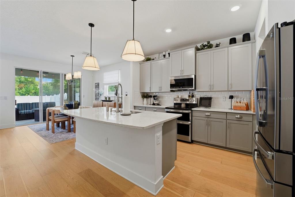 A modern kitchen features a large white island, gray cabinetry, stainless steel appliances, and wood flooring — 8020 PRAISE DRIVE, TAMPA, FL