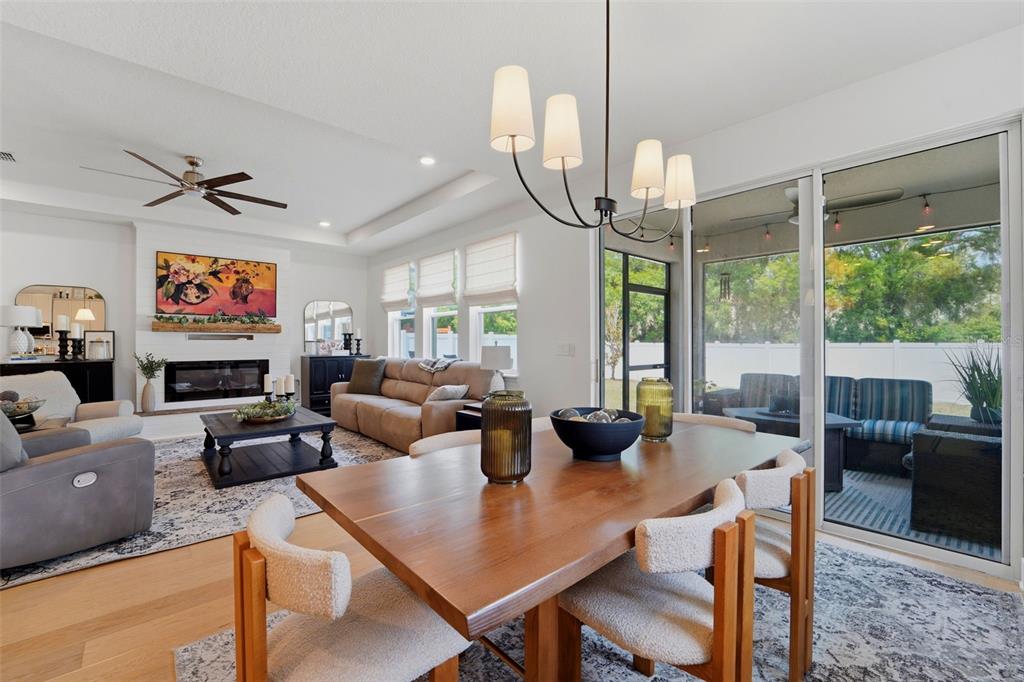 An open-concept living and dining area features a fireplace, wood floors, and sliding glass doors — 8020 PRAISE DRIVE, TAMPA, FL