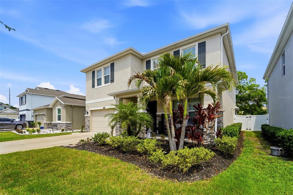 A two-story suburban house with a tan stucco exterior, a two-car garage, and palm trees — 8020 PRAISE DRIVE, TAMPA, FL