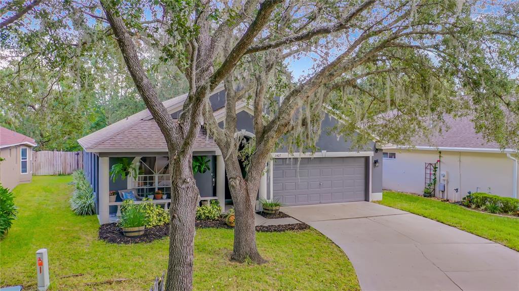 A single-story house with a gray garage, a covered front porch, and large oak trees — 1407 TRAIL BOSS LANE, BRANDON, FL