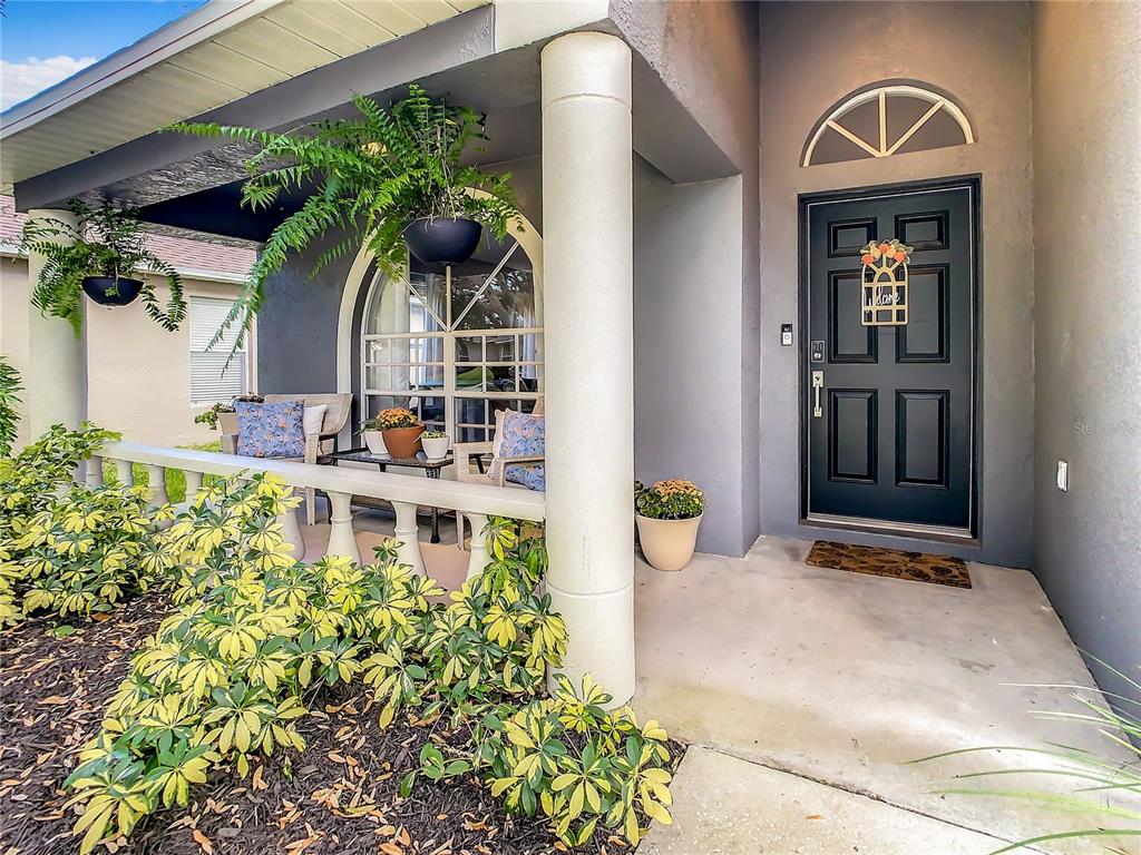 A covered front porch features a dark door, arched window, and potted plants — 1407 TRAIL BOSS LANE, BRANDON, FL