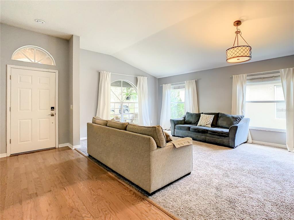A living room features a tan sofa, a dark gray sofa, carpeted flooring, and a chandelier — 1407 TRAIL BOSS LANE, BRANDON, FL