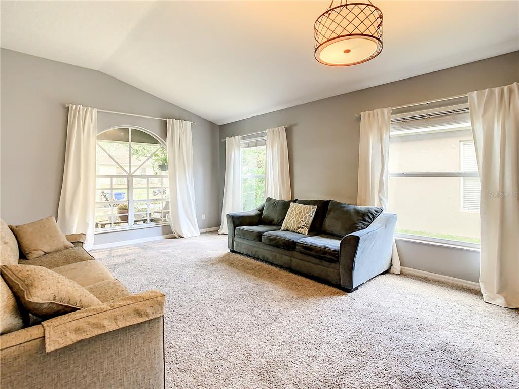 A living room features gray walls, carpeted flooring, two sofas, and large windows with curtains — 1407 TRAIL BOSS LANE, BRANDON, FL