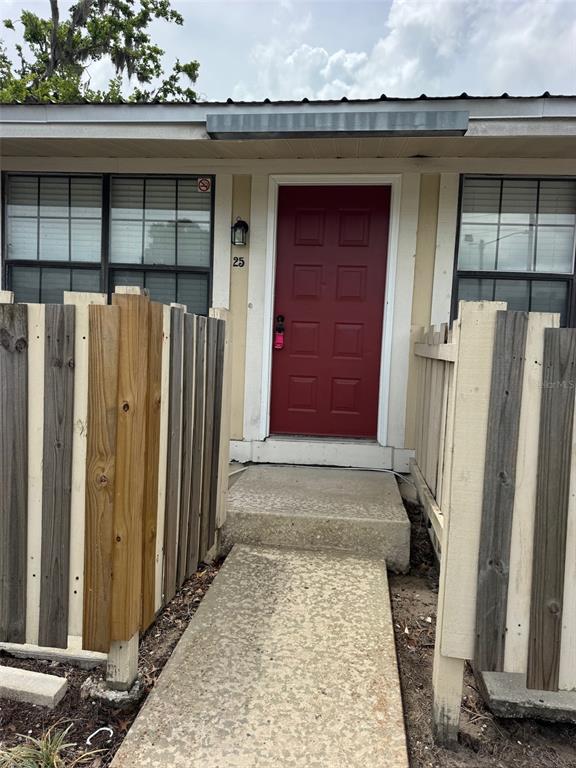 A red front door is centered between two windows and flanked by wooden privacy fences — 420-420 MILLS STREET UNIT 25, LEESBURG, FL