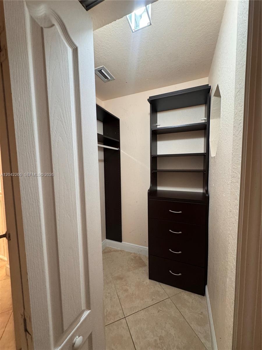 A walk-in closet features dark wood shelving, a four-drawer dresser, and beige tile flooring — 8810 W Flagler St # 11, Miami FL 33174, MIAMI, FL
