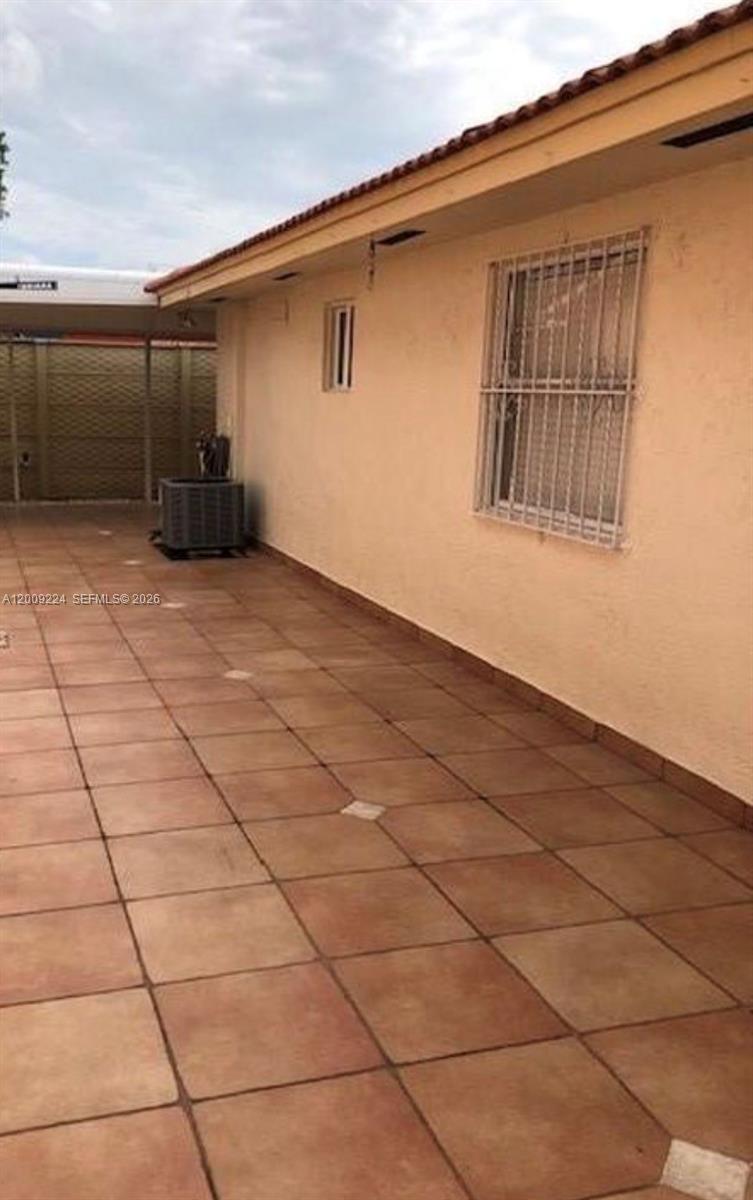 A tiled patio area runs alongside a beige exterior wall with a window and security bars — HIALEAH GARDENS, FL