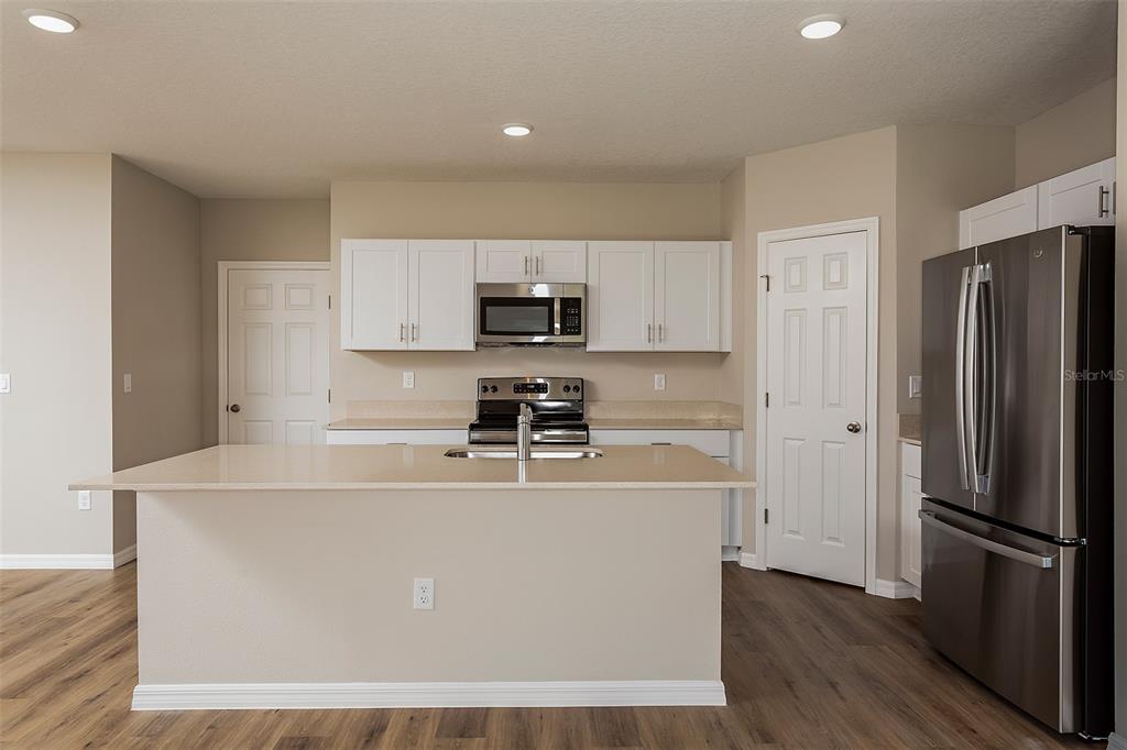 A kitchen features a central island, white cabinets, stainless steel appliances, and wood-look flooring — 33631 NOBLE CREEK PLACE, DADE CITY, FL