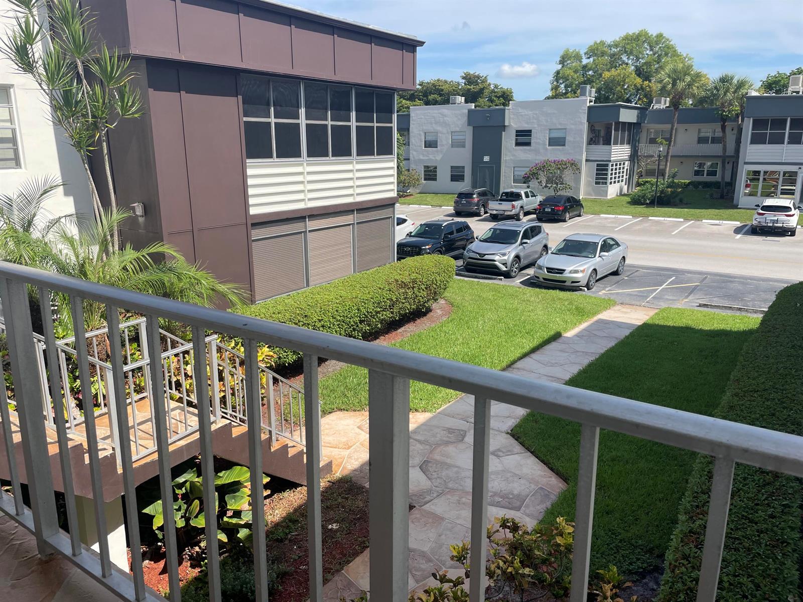 A view from a balcony overlooking a landscaped courtyard, parking lot, and apartment buildings — 705 Normandy O # 705, Delray Beach FL 33484, DELRAY BEACH, FL