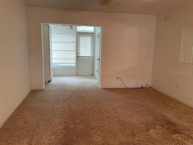 A carpeted living room leads to a sunroom with a glass door and blinds — 120B E MINNESOTA AVENUE UNIT B, DELAND, FL