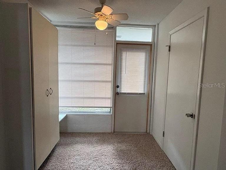 A small room with carpeted flooring, a ceiling fan, a large window, and two doors — 120B E MINNESOTA AVENUE UNIT B, DELAND, FL