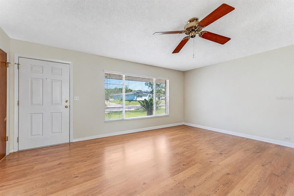 An empty living room with light-colored walls, wood-look flooring, a ceiling fan, and a window — 1106 BLUEBERRY DRIVE, PORT ORANGE, FL