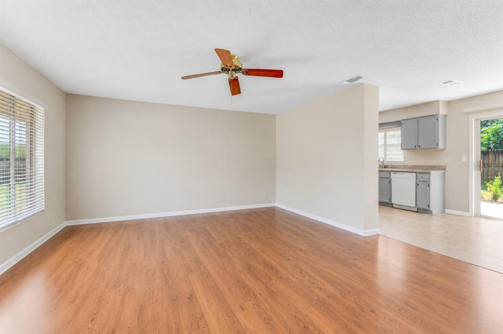 An empty living room with wood-look flooring and a ceiling fan opens to a kitchen — 1106 BLUEBERRY DRIVE, PORT ORANGE, FL
