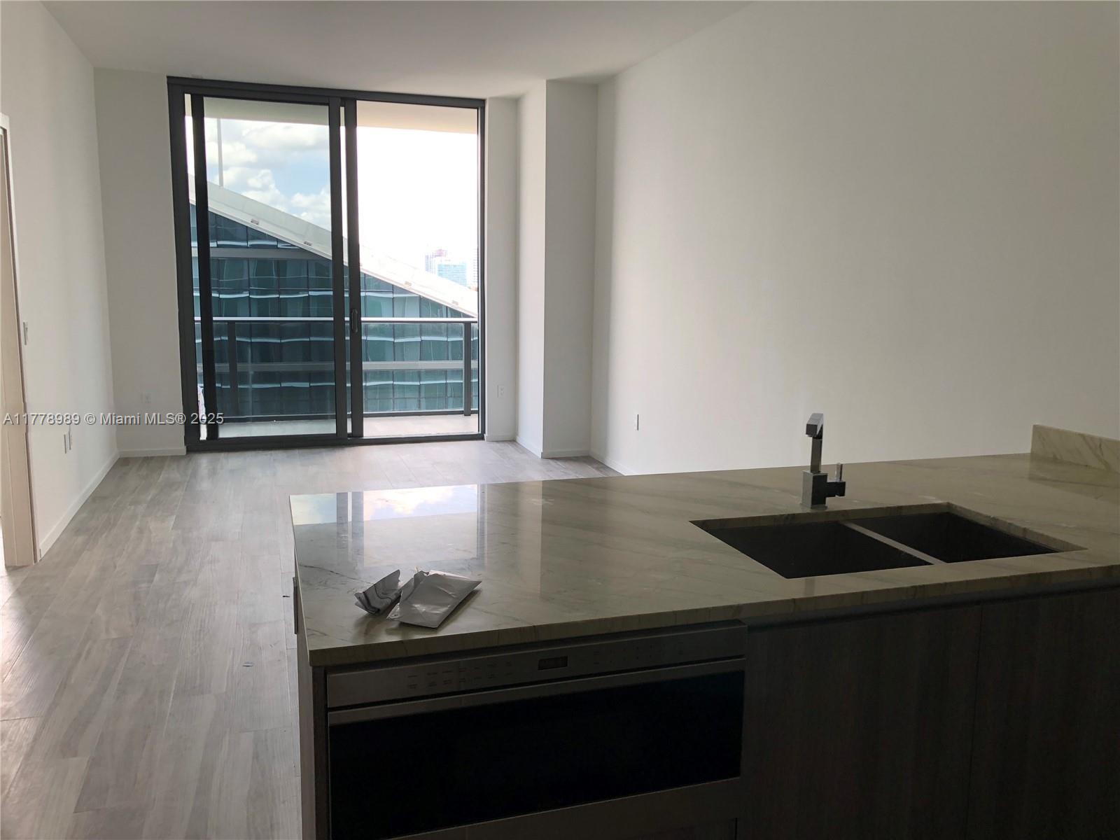 A modern kitchen island with a sink faces a living area with sliding glass balcony doors — 801 S Miami Ave # 5108, Miami FL 33130, MIAMI, FL